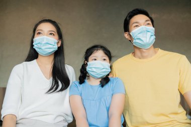 Cerrahi koruyucu yüz maskesi takan güçlü sağlıklı Asyalı aile yeni normal yaşam tarzını bozmak için evlerinde bir arada kalıyorlar.