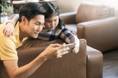 Genç mutlu Asyalı aile el resmi neşeli ve eğlenceli karantina dönemi yeni normal yaşam tarzı, anne ve baba oturma odasındaki kanepede birlikte fotoğraf çekiyorlar.