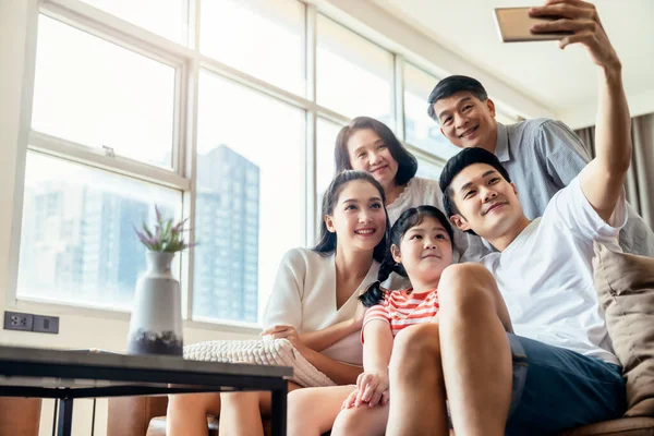 亚洲多代父母和祖父母带着小女儿坐在客厅的沙发上放松一下 在家里 你可以拿着智能手机 — 图库照片