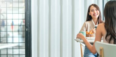 Çekici Asyalı bir kadın arkadaşlarıyla konuşurken gülümseyen gülüşü ve mutluluğu olan arkadaşlarıyla kafenin penceresinin yanında gün ışığıyla bahçedeki pozitif tutum ilişkisinden.