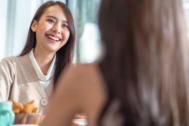Çekici Asyalı bir kadın arkadaşlarıyla konuşurken gülümseyen gülüşü ve mutluluğu olan arkadaşlarıyla kafenin penceresinin yanında gün ışığıyla bahçedeki pozitif tutum ilişkisinden.