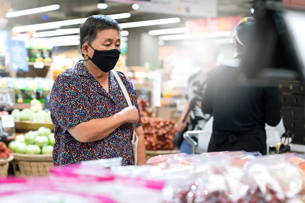 old senior asian woman wear virus spread protection mask while shopping fresh vagetable and fruit at grocery store in supermarket new normal lifestyle after lockdown is over