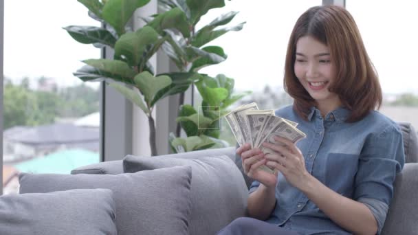 亚洲迷人的女性快乐而快乐的手捧着钞票笑着在客厅的沙发上离去 — 图库视频影像