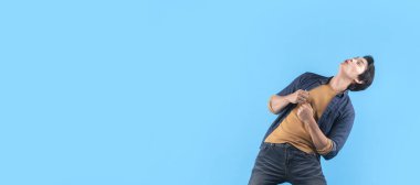 Neşeli Asyalı erkek, başparmağının boş olduğunu işaret ediyor. El hareketi, parmak işareti, geniş gülümseme, açık ağız, günlük kumaş pantolon, izole edilmiş mavi arka plan.