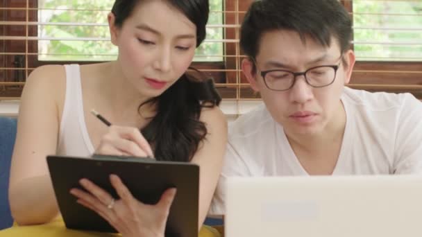Handheld szerokie ujęcie azjatyckiego małżeństwa para robi finanse na tablecie cyfrowym laptop w salonie tło domu — Wideo stockowe