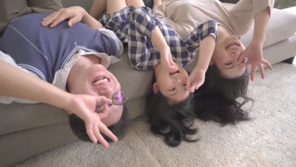 Zpomalení film šťastný asijské rodina matka otec a dcera dělat zábavu spánek vzhůru nohama na pohovce obývací pokoj domácí pozadí. — Stock video