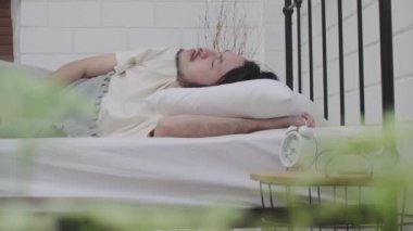 Tembel, çok çalışan, beyaz yataktaki Asyalı adam uyanmak için can atıyor.