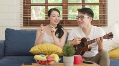 Genç Asyalı mutlu bir çiftle ukulele oynayarak ve oturma odasında şarkı söyleyerek evleniyor. Mutlu çift hafta sonu evde dinleniyor.