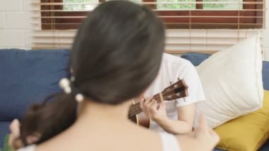 Genç Asyalı mutlu bir çiftle ukulele oynayarak ve oturma odasında şarkı söyleyerek evleniyor. Mutlu çift hafta sonu evde dinleniyor.