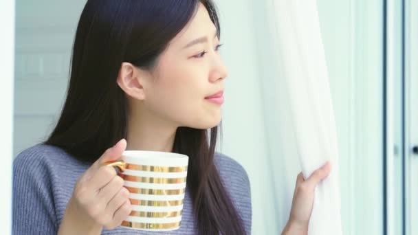 아름다운 아시아 여인 은방에서 창문에 불을 켜 놓고 따끈 한 음료를 마시며 아침 시간을 즐긴다 — 비디오