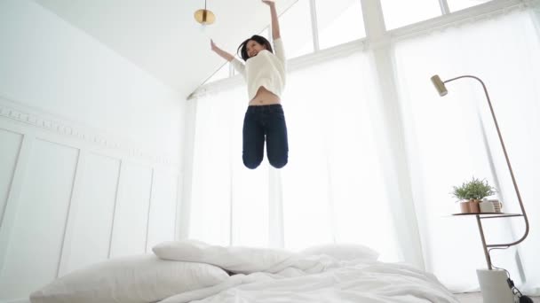 Slow motion of exited asian woman jump over white bed in bedroom with energy and happiness success lifestyle ideas concept — Stock Video