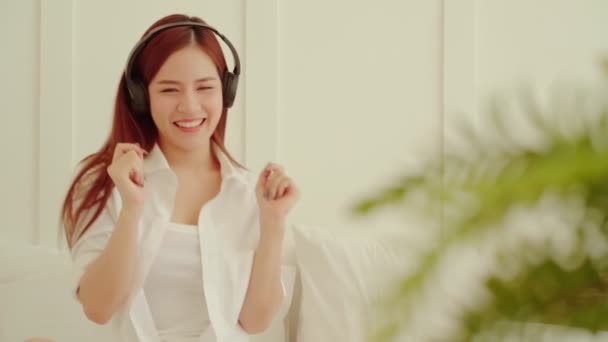 Atraktivní asijské krásná žena těšit tanec s melodií z sluchátka víkendové aktivity na posteli bílá ložnice interiér pozadí — Stock video