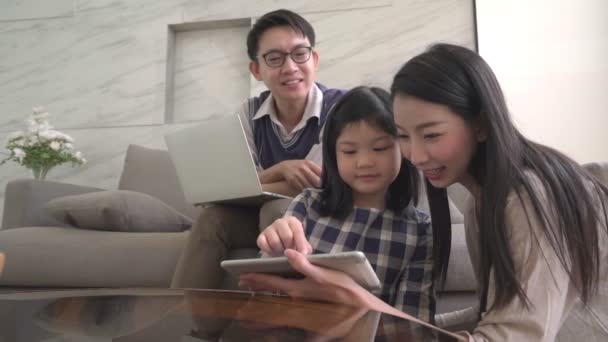 Zwolniony ruch azjatycka córka robi pracę domową na notatniku. Jego rodzice siedzą i oglądają na sofie i używają laptopa cyfrowego razem w domu.. — Wideo stockowe