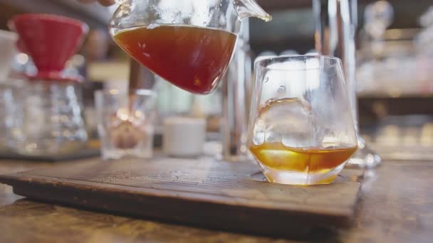 Koude koffie zetten in een fles met ijsblokjes in een glazen tuimelaar op een houten tafel van boven. Een fles koud gebrouwen koffie en ijs in glas bereidend Cold Brew drankje. — Stockvideo