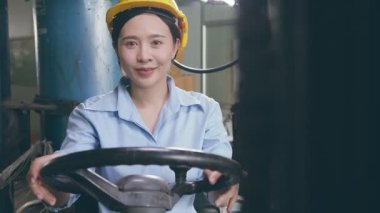 Mutluluk gülümseyen Asyalı kadın işçi kasklı depo fabrikasında forklift kullanıyor.