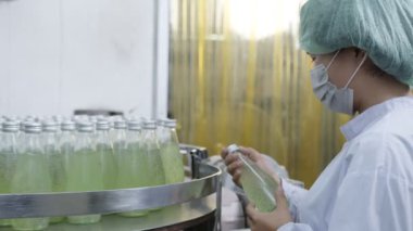 Asyalı kadın denetçi içki fabrikasında bir şişe bitki içeceği üretim hattını teftiş ediyor. Kadın işçi, içki üretimini kontrol ediyor. Fabrika endüstriyel konsepti.