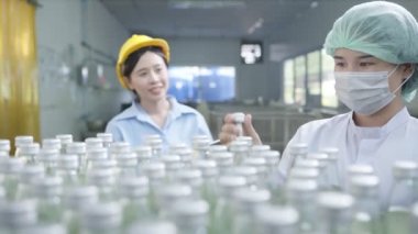Asyalı kadın denetçi içki fabrikasında bir şişe bitki içeceği üretim hattını teftiş ediyor. Kadın işçi, içki üretimini kontrol ediyor. Fabrika endüstriyel konsepti.