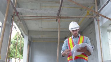 Bölge müfettişliğindeki genç beyaz mühendis meslektaşları ve birlikte inşaat alanındaki dizüstü bilgisayar ve kağıt taslakları kullanarak ev yenileme fikirleri kavramını tartışıyorlar.