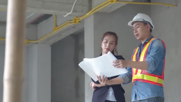 Giovane gestore del sito femminile asiatico consultarsi con i colleghi ingegnere ispettore del sito e discutere insieme utilizzando carta cianografia in cantiere. — Video Stock