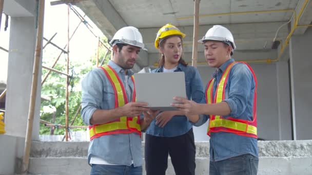 Mladí asijští inženýři a kolegové z kavkazského inženýra na staveništi společně diskutují pomocí notebooku a papírového nákresu na staveništi. — Stock video