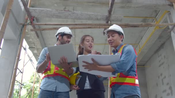 Asyalı genç mühendisler ve bölge müfettişindeki beyaz mühendis meslektaşları inşaat alanındaki dizüstü bilgisayar ve kağıt şablonu kullanarak tartışıyorlar. Ev yenileme fikirleri kavramı — Stok video