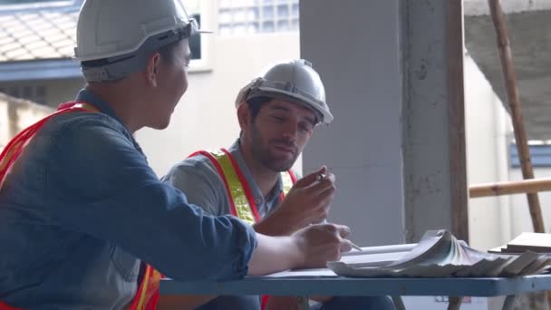 Jonge Aziatische ingenieurs en blanke ingenieurs collega 's op site inspecteur en bespreken samen met behulp van notebook computer en papier blauwdruk op bouwplaats.home renovatie ideeën concept — Stockvideo