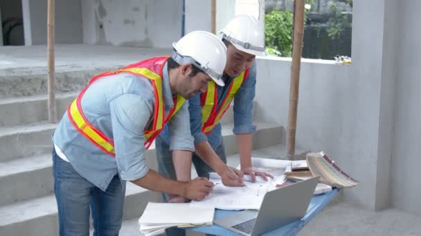 Jonge Aziatische ingenieurs en blanke ingenieurs collega 's op site inspecteur en bespreken samen met behulp van notebook computer en papier blauwdruk op bouwplaats.home renovatie ideeën concept — Stockvideo