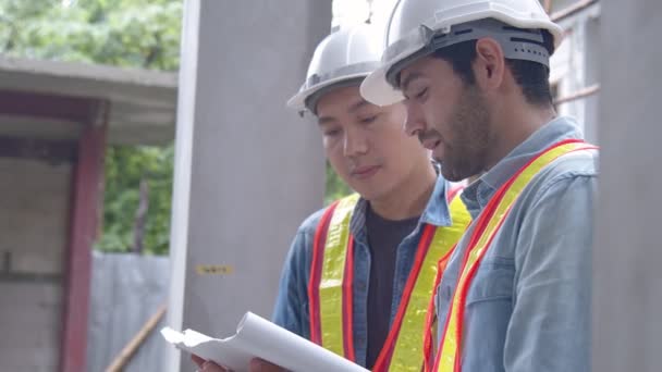 Молоді азійські інженери та колеги-початківці на місці інспектора обговорюють разом за допомогою ноутбука і паперового креслення на будівництві. — стокове відео