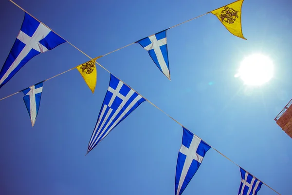 Steaguri grecești triunghiulare pe cer albastru, soare — Fotografie, imagine de stoc