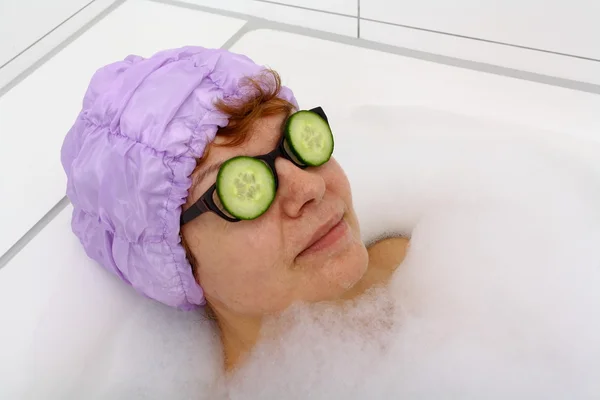 Femme mûre dans la baignoire avec des tranches de concombre sur les lunettes — Photo