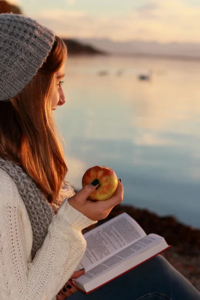 Happy girl sitting with book and apple on lake — Stock Photo, Image