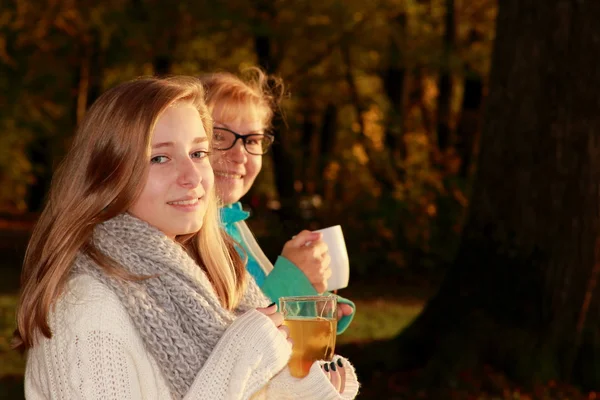 Daughter and mother drink tea in autumn park — Stock Photo, Image