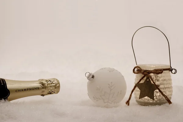 Bola de Navidad, vela de viento, botella de champán en la nieve —  Fotos de Stock