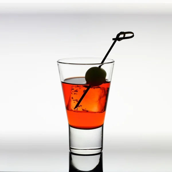 Short drink glass with red liquid, olive, ice cubes — Stock Photo, Image