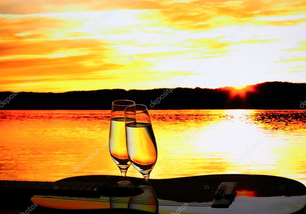 Two champagne glasses with guitar at sunset
