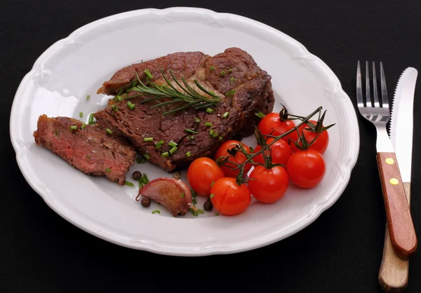 Rib eye steak, garlic, cherry tomatoes, herbs on black — Stock Photo, Image