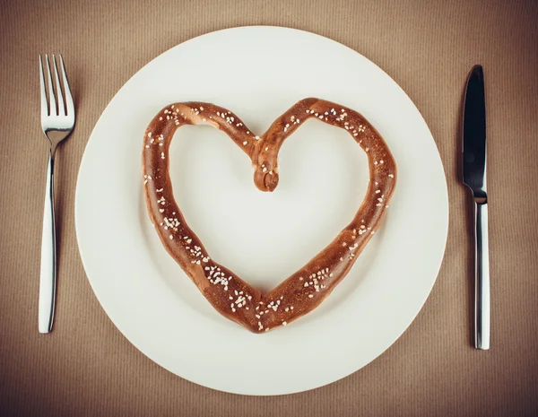 Pretzel in heart shaped on plate with cutlery — Stock Photo, Image