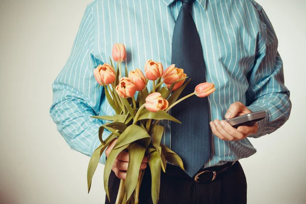 Geschäftsmann wählt Telefonnummer mit Tulpen in der Hand — Stockfoto