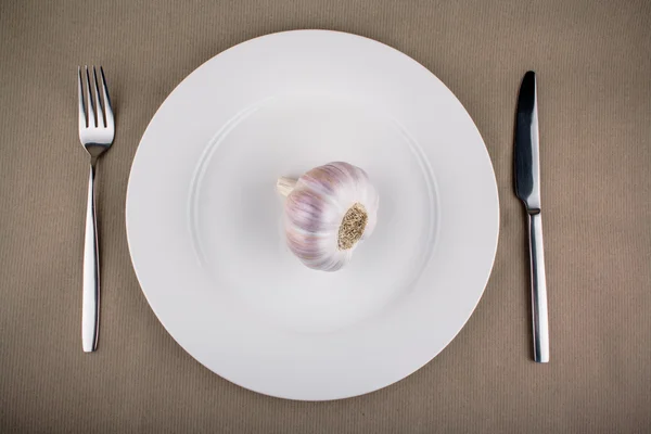 Garlic on white plate with fork and knife — Stock Photo, Image