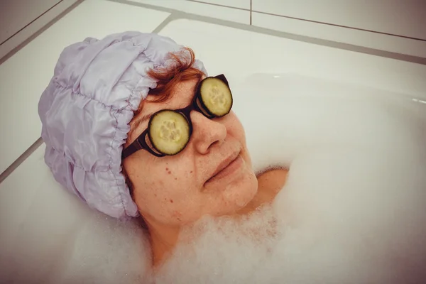 Femme mûre dans la baignoire avec des tranches de concombre sur les lunettes — Photo