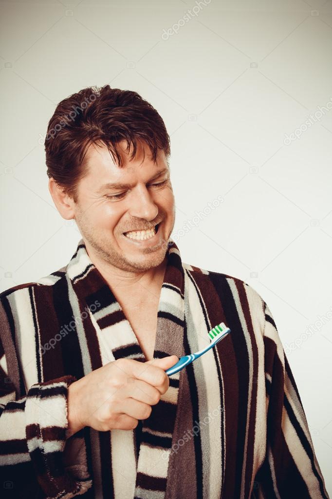 Young man in bathrobe brushing teeth, toned