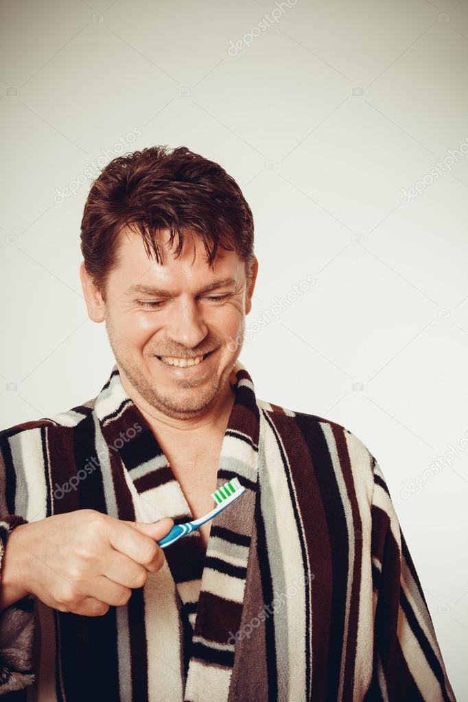 Smile man in bathrobe brushing teeth