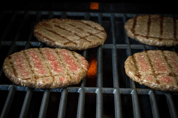 Four beef hamburger slices on grill rack, soft focus — ストック写真