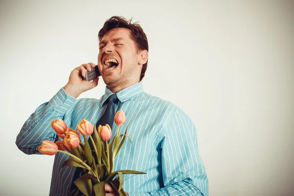 Uomo d'affari sorridente mentre telefona e tiene tulipani — Foto Stock