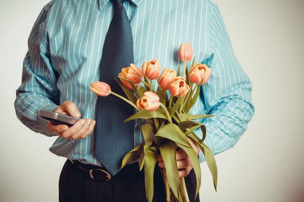Empresário enquanto telefona e segura tulipas — Fotografia de Stock