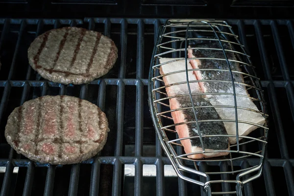 Duas fatias de hambúrguer e bife de salmão no grelhador — Fotografia de Stock