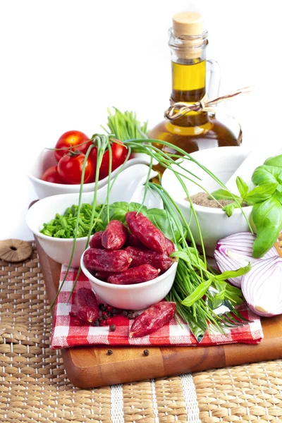 Salsicce con pomodori, verdure e olio d'oliva su una tavola di legno — Foto Stock