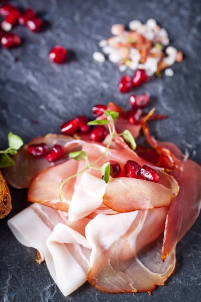 Sliced prosciutto with herbs and pomegranate seeds — Stock Photo, Image