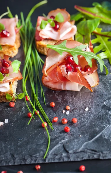 Sliced prosciutto with herbs and pomegranate seeds — Stock Photo, Image