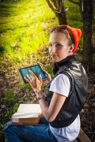 Woman in park outdoor with tablet and book deciding what to use — Stock Photo, Image